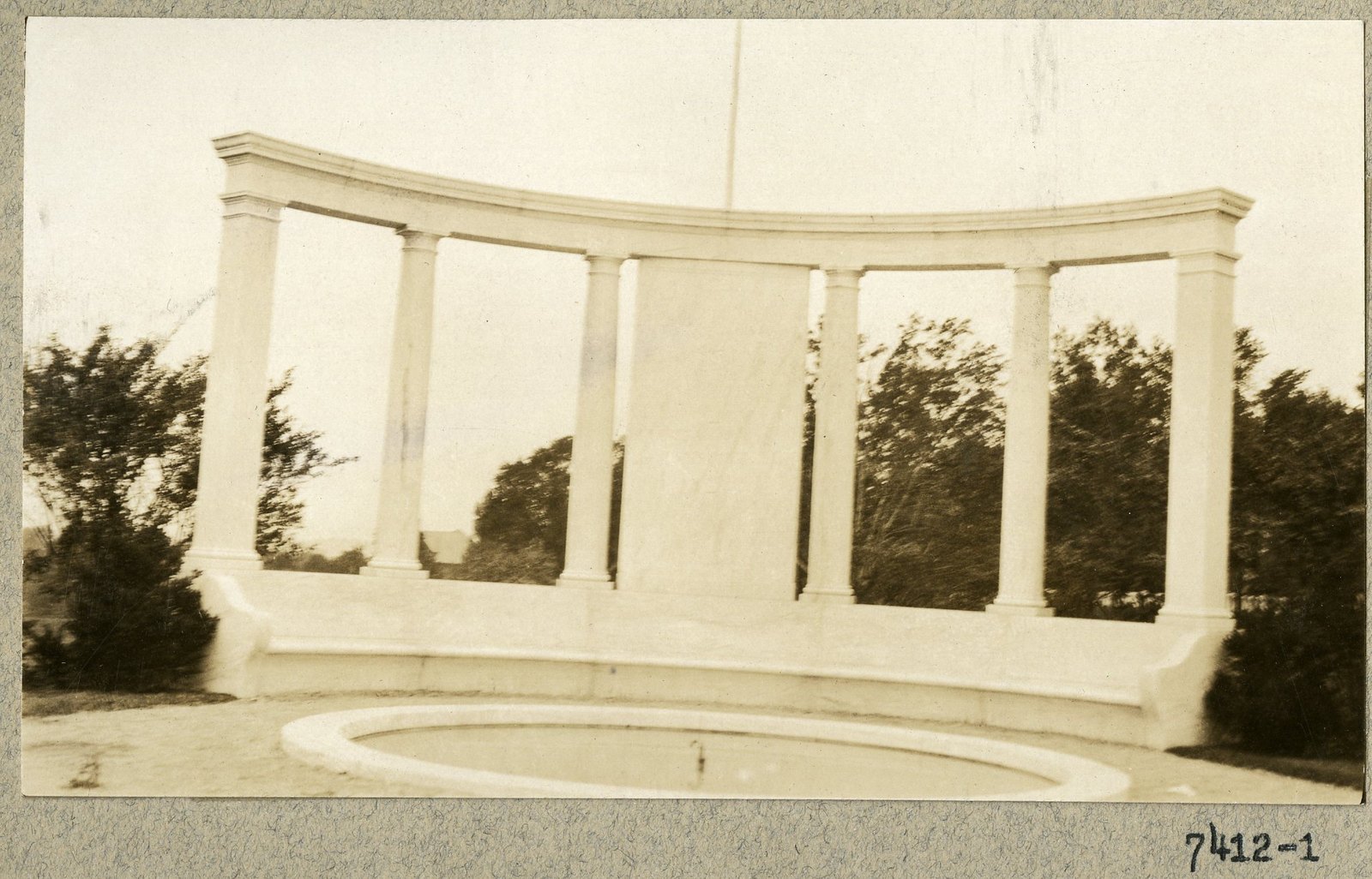 Print 7412-1 from the office album: the memorial as built — a curved marble colonnade with its fountain basin.