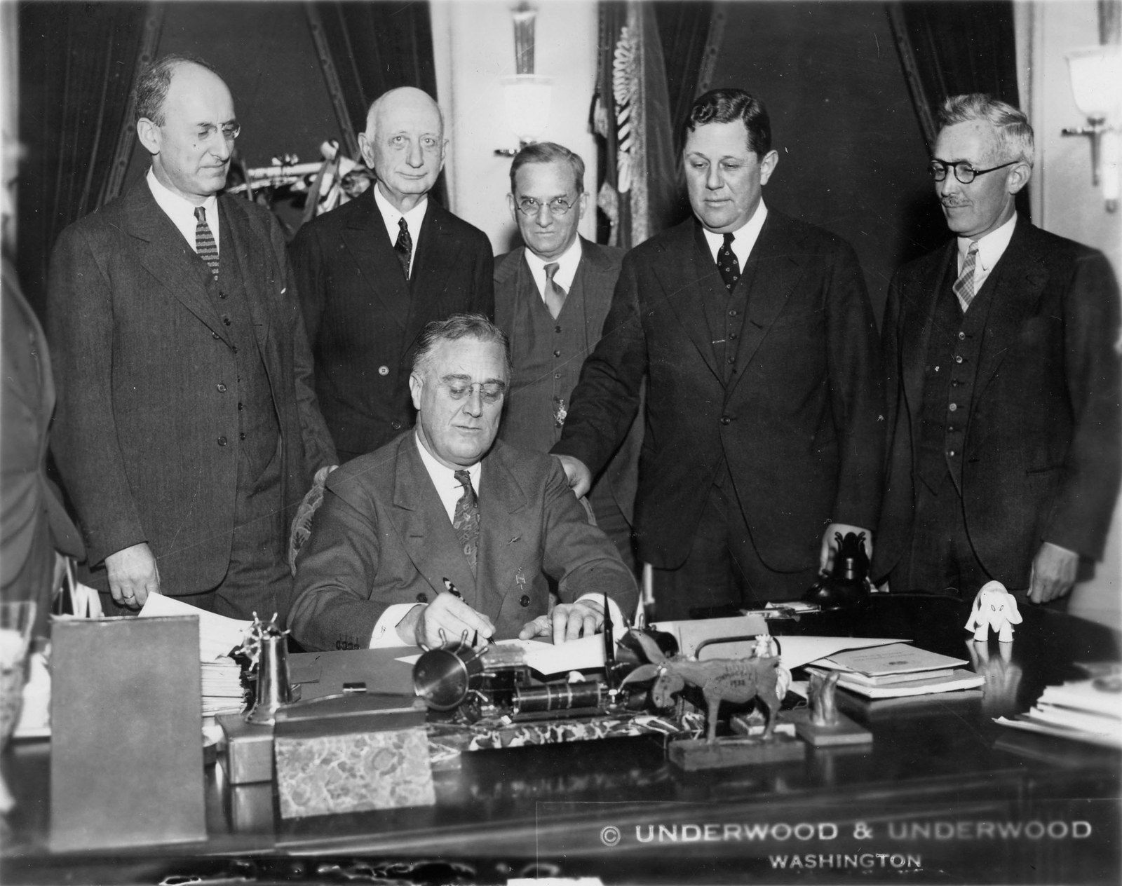 Roosevelt signing the Gold Reserve Act, 30 January 1934. It moved all monetary gold to the Treasury, revalued the dollar from $20.67 to $35 the ounce, and required that monetary gold be held as bars. Coins were forbidden.