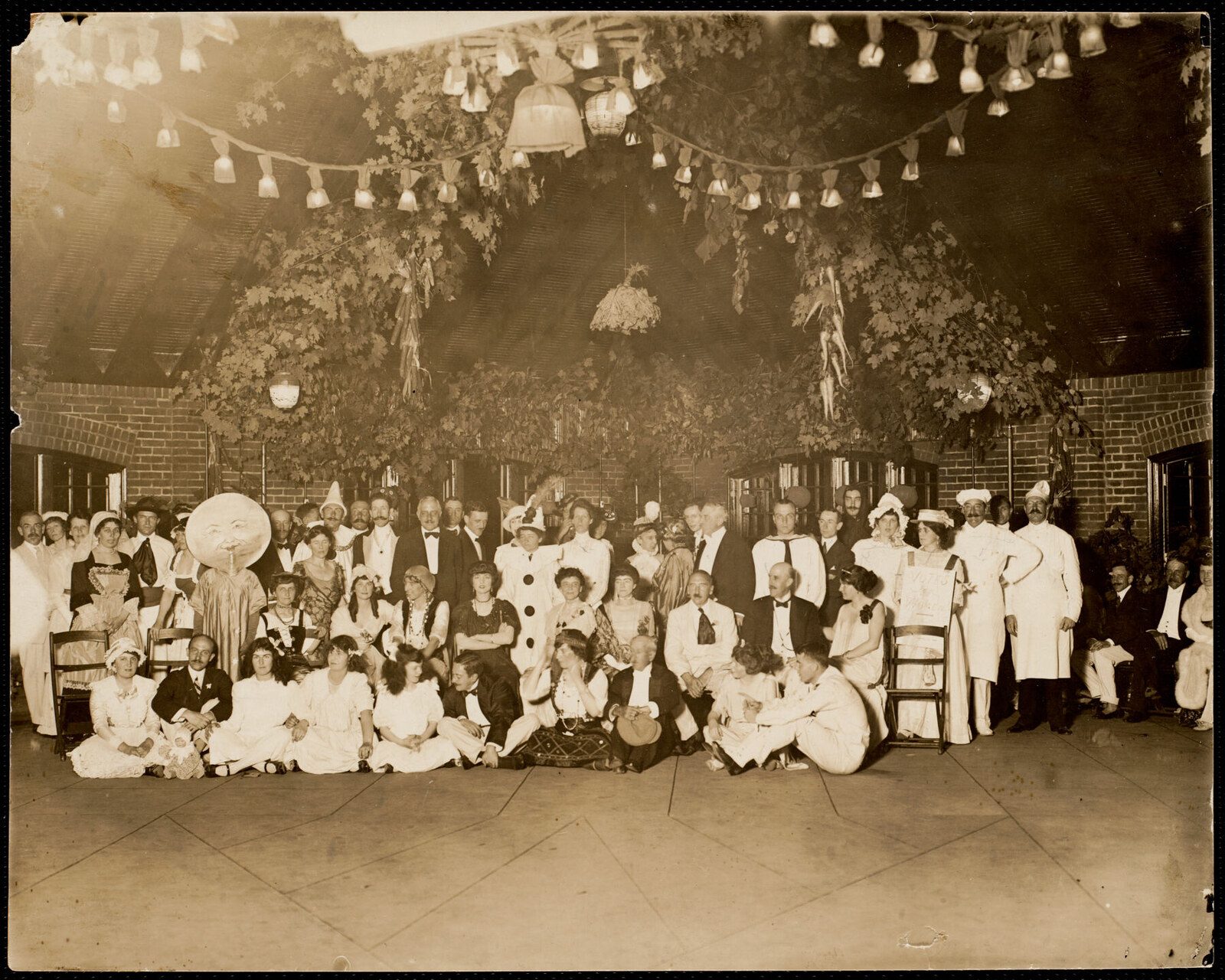 Catalogued as “Hallowe’en party at Highlawn,” about 1910. Sixty-odd people in fancy dress under paper lanterns and maple boughs, in a brick-walled room with an open timber roof.