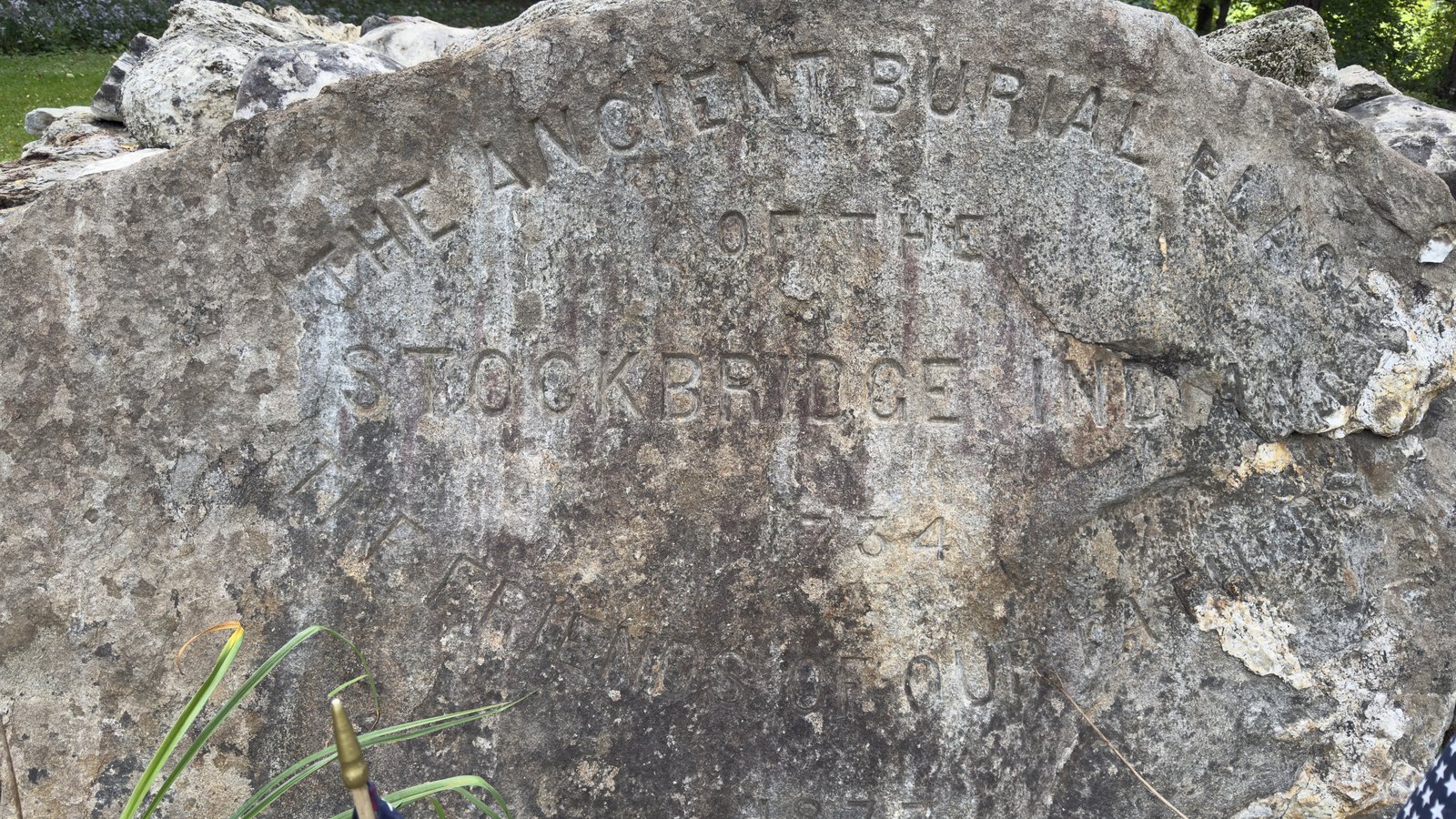 The inscribed boulder at the foot of the monument, transcribed as cut: THE ANCIENT BURIAL PLACE / OF THE / STOCKBRIDGE INDIANS / 1734 / THE FRIENDS OF OUR FATHERS / 1877. The photograph crops the right-hand end of the longer lines.