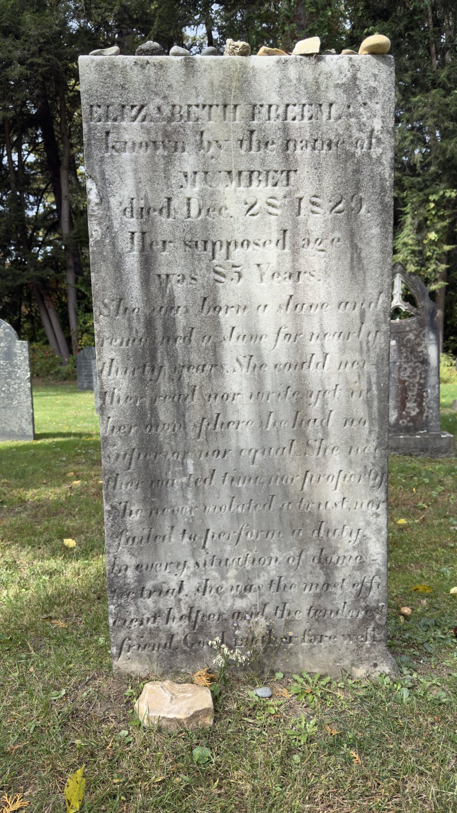 Elizabeth Freeman’s stone, transcribed as cut, with the line breaks as they fall: ELIZABETH FREEMAN / known by the name of / MUMBET / died Dec. 28 1829. / Her supposed age / was 85 Years. / She was born a slave and / remained a slave for nearly / thirty years. She could nei- / ther read nor write yet in / her own sphere she had no / superior nor equal. She nei- / ther wasted time nor property / She never violated a trust, nor / failed to perform a duty. / In every situation of domes- / tic trial, she was the most effi- / cient helper and the tenderest / friend. Good mother fare well.