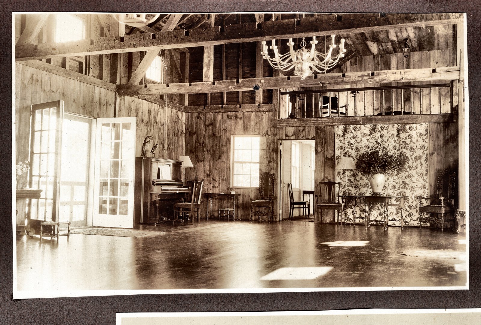 The converted barn at Orleton Farm: French doors to the lawn, plain board walls, and a chandelier under the original framing.