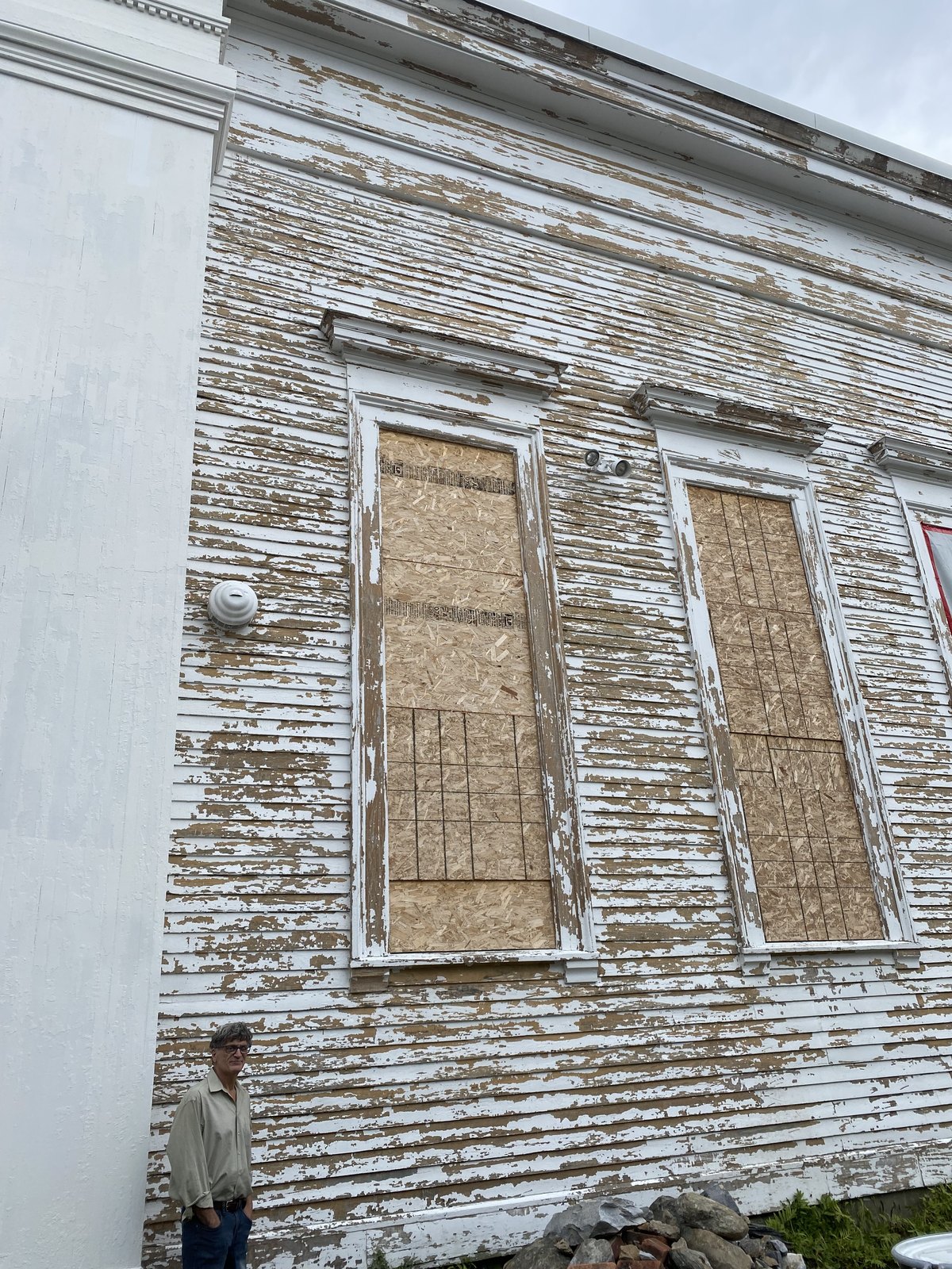 The south elevation before work, paint gone to bare wood and the windows blinded with board.