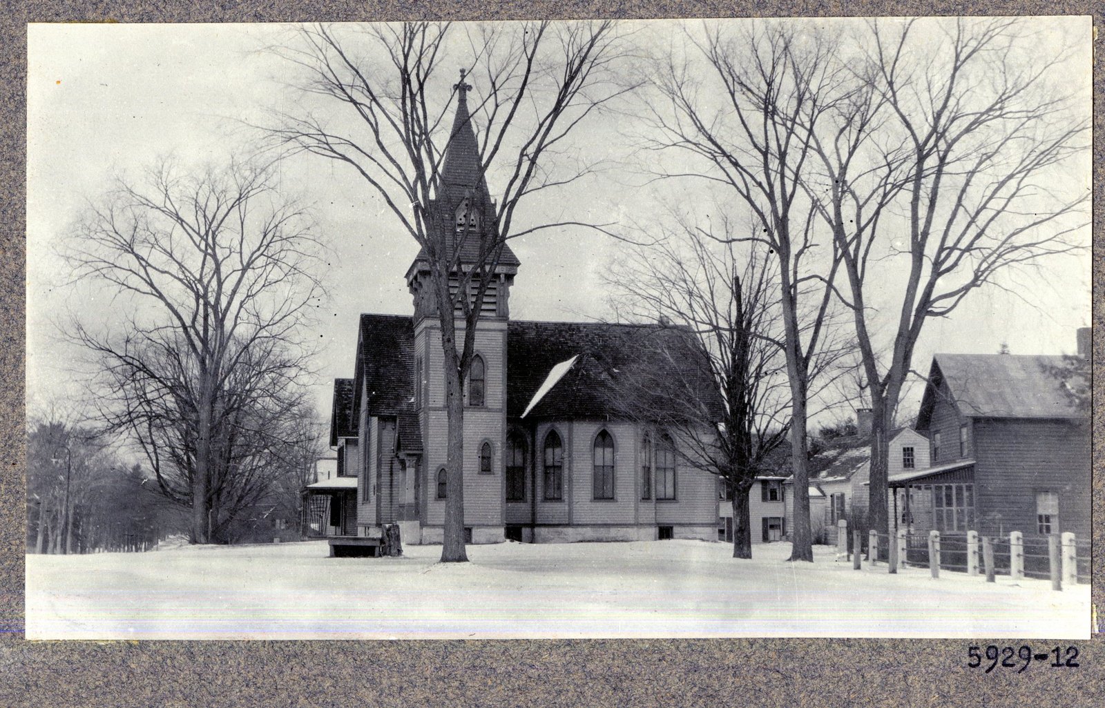 Print 5929-12. No typed caption; the number only. A shingled church with a spired tower, in snow, with houses beyond and a post-and-rail fence at the right.