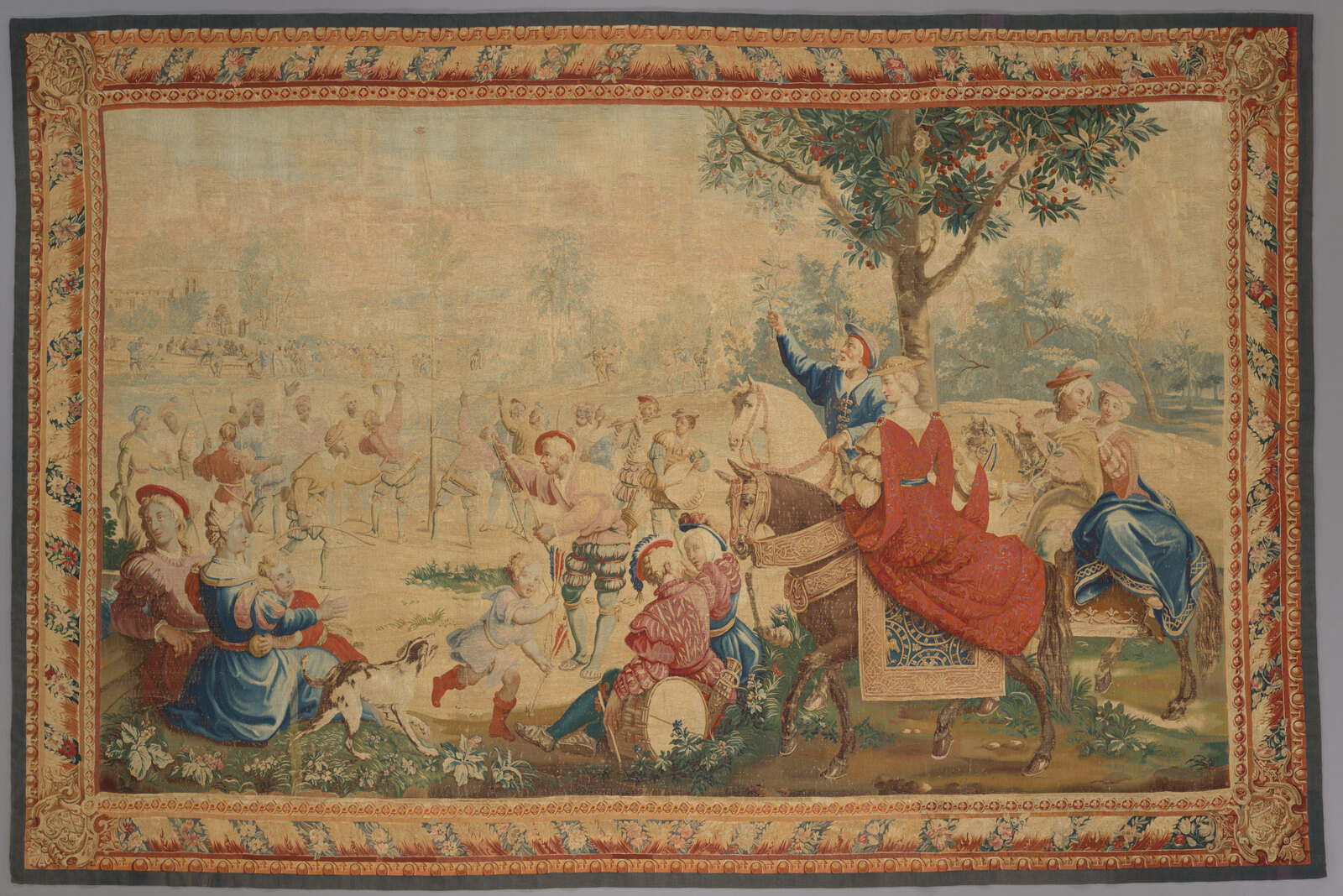 A May Day festival, woven in France some time between 1723 and 1774 — archers shooting at a bird on a maypole, spectators on horseback, a border of rolled acanthus. This is the eighteenth-century manner: a painting, in wool.